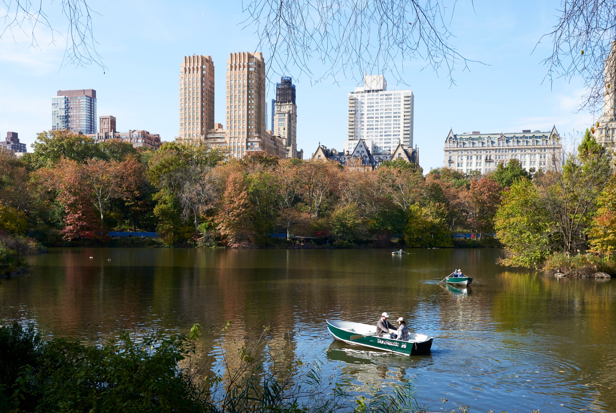 Boats on a Central Park lake with apartment towers beyond autumn trees