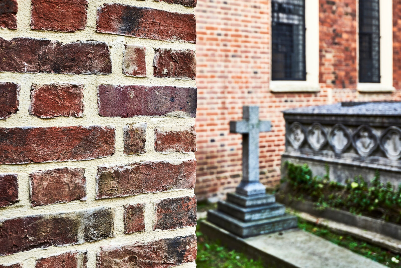 Brick corner in close focus with church windows and a gravestone beyond