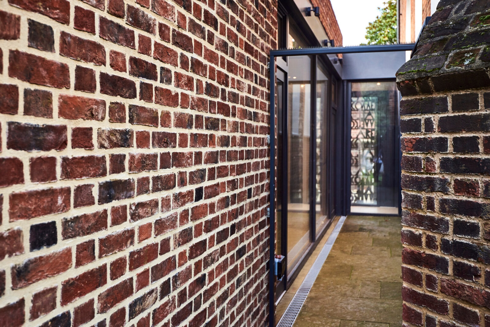 Narrow passage leading through a glazed opening beside historic brickwork
